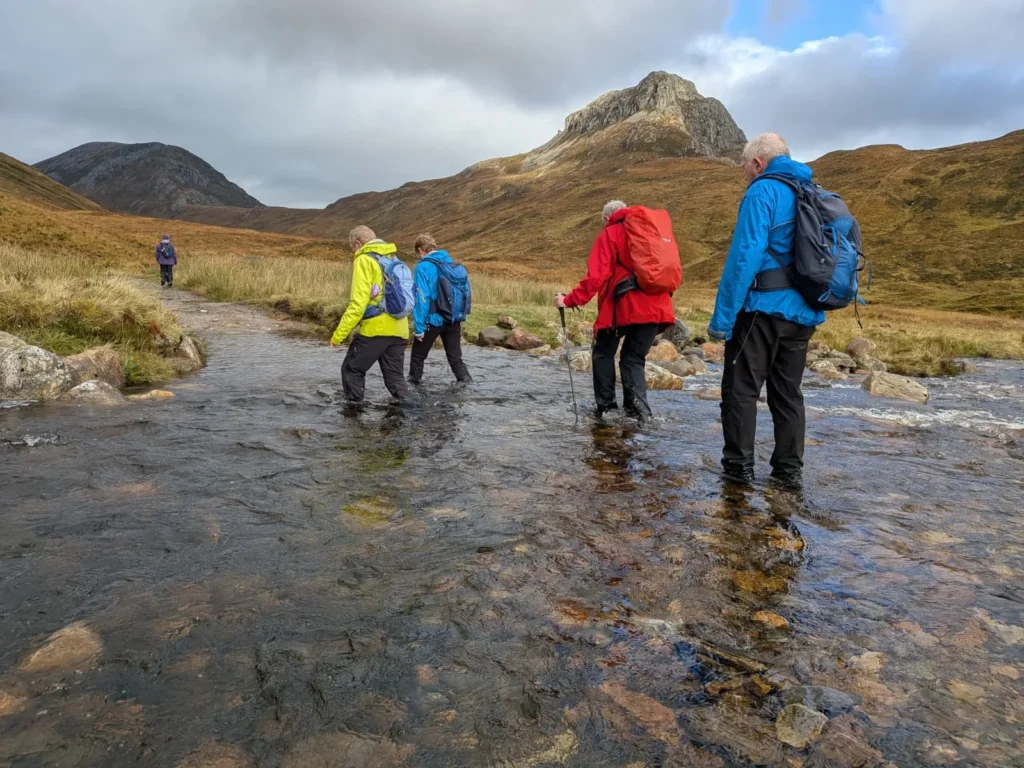 Walkers wading a river crossing in the Lairig Leacach